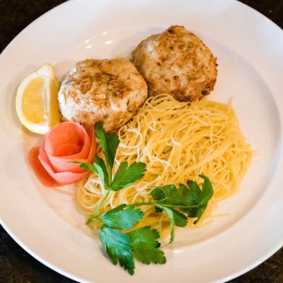 2 crab cakes, pasta served on a white plate.